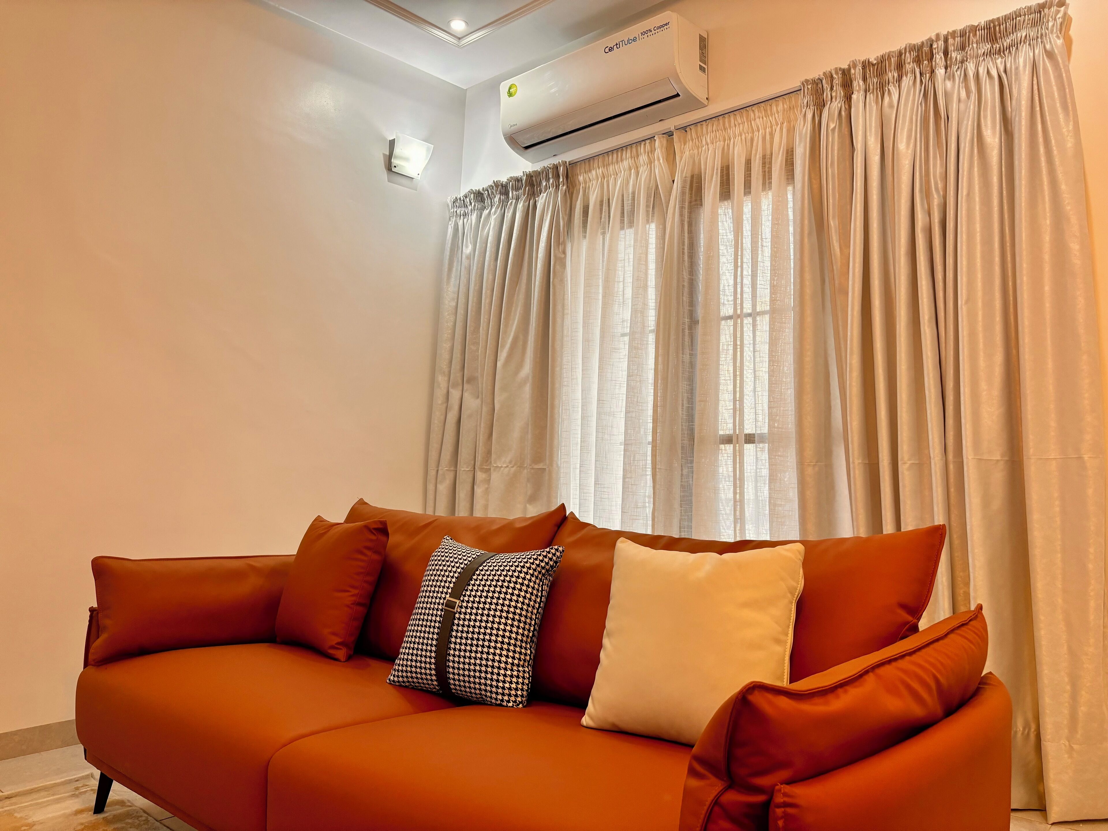A living room with a sofa, air conditioning unit, and sheer curtains.