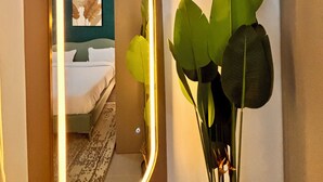 Une chambre d’hôtel avec un lit, un miroir avec un éclairage intégré et une plante.