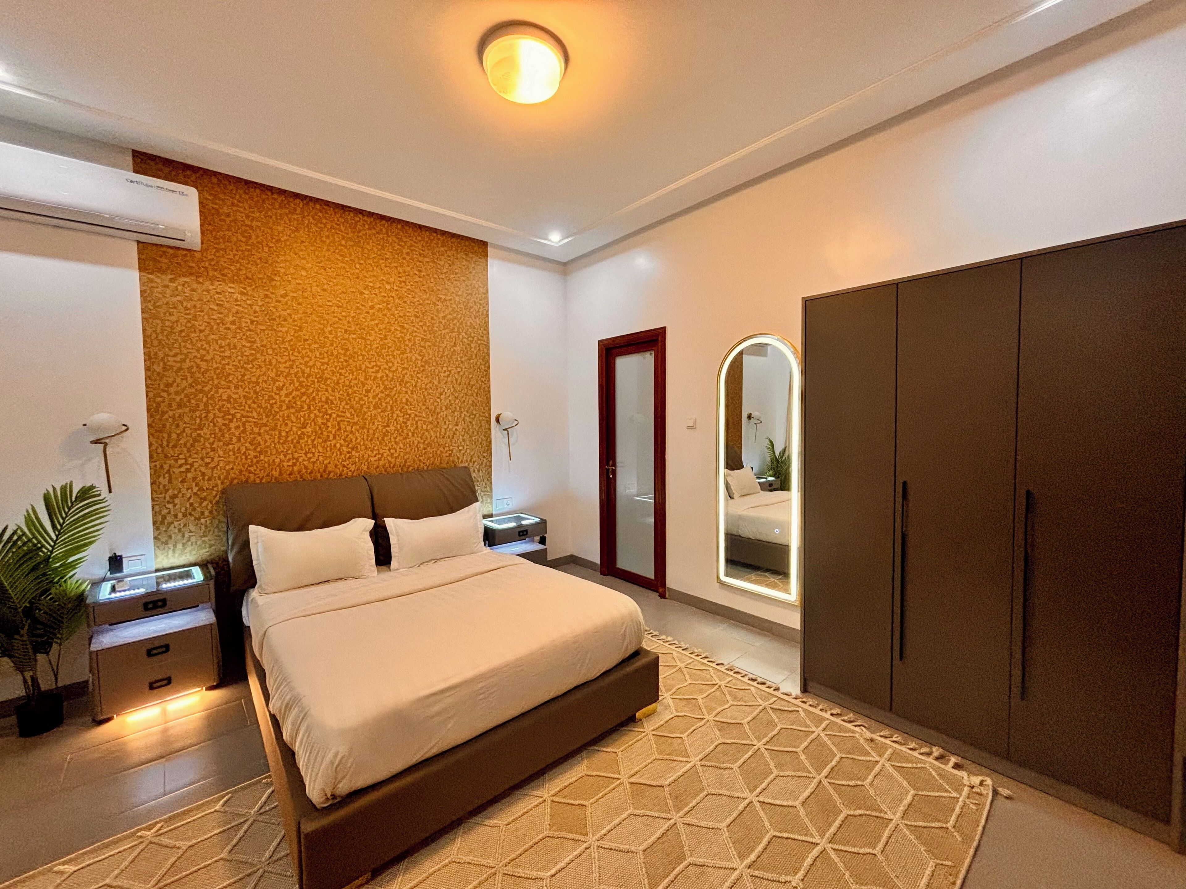 A modern bedroom with a large bed, a wardrobe, a mirror, and a wall-mounted air conditioner.