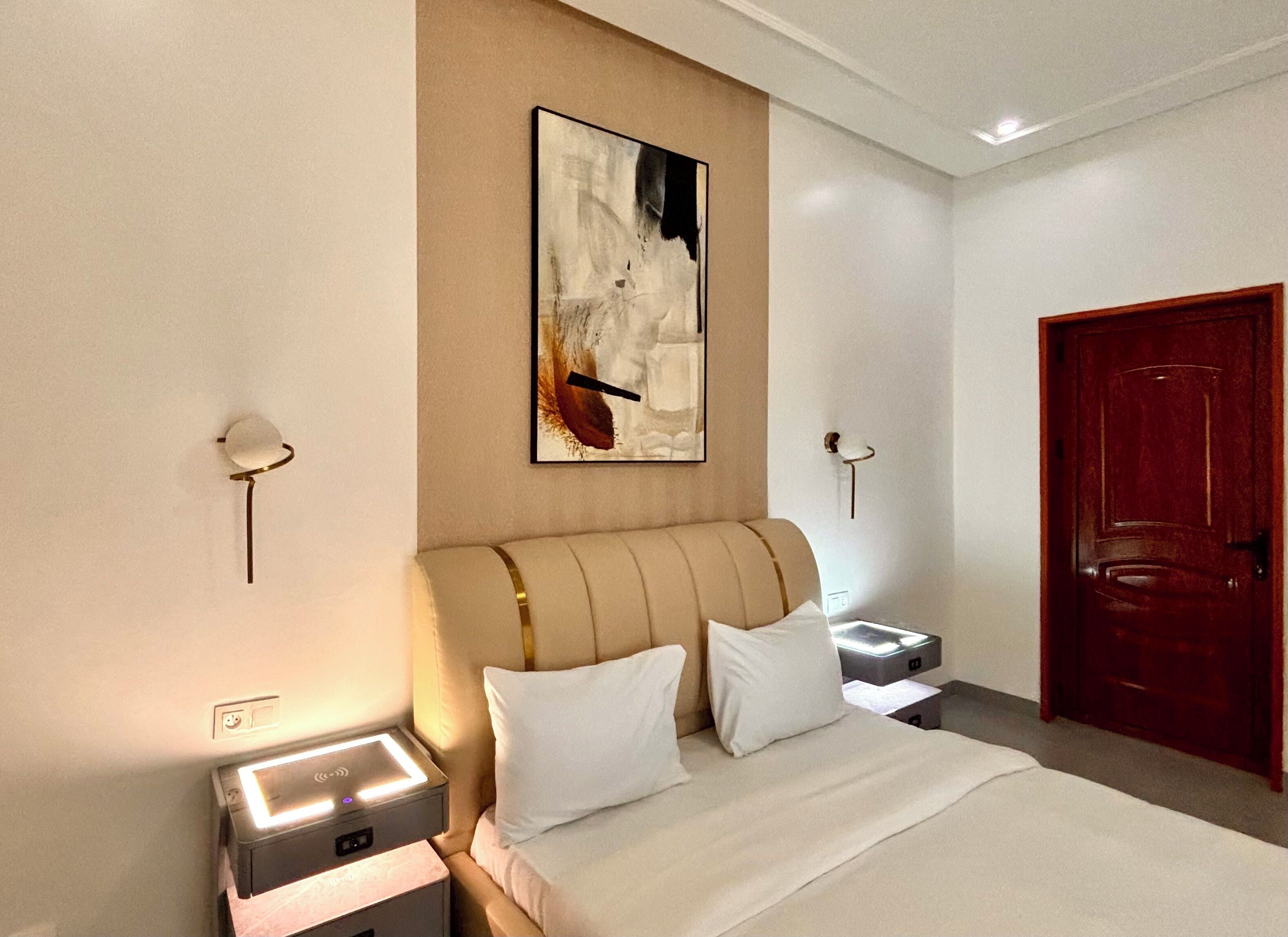 Una habitación de hotel con una cama, mesitas de noche, una puerta roja y un cuadro abstracto colgado en la pared.