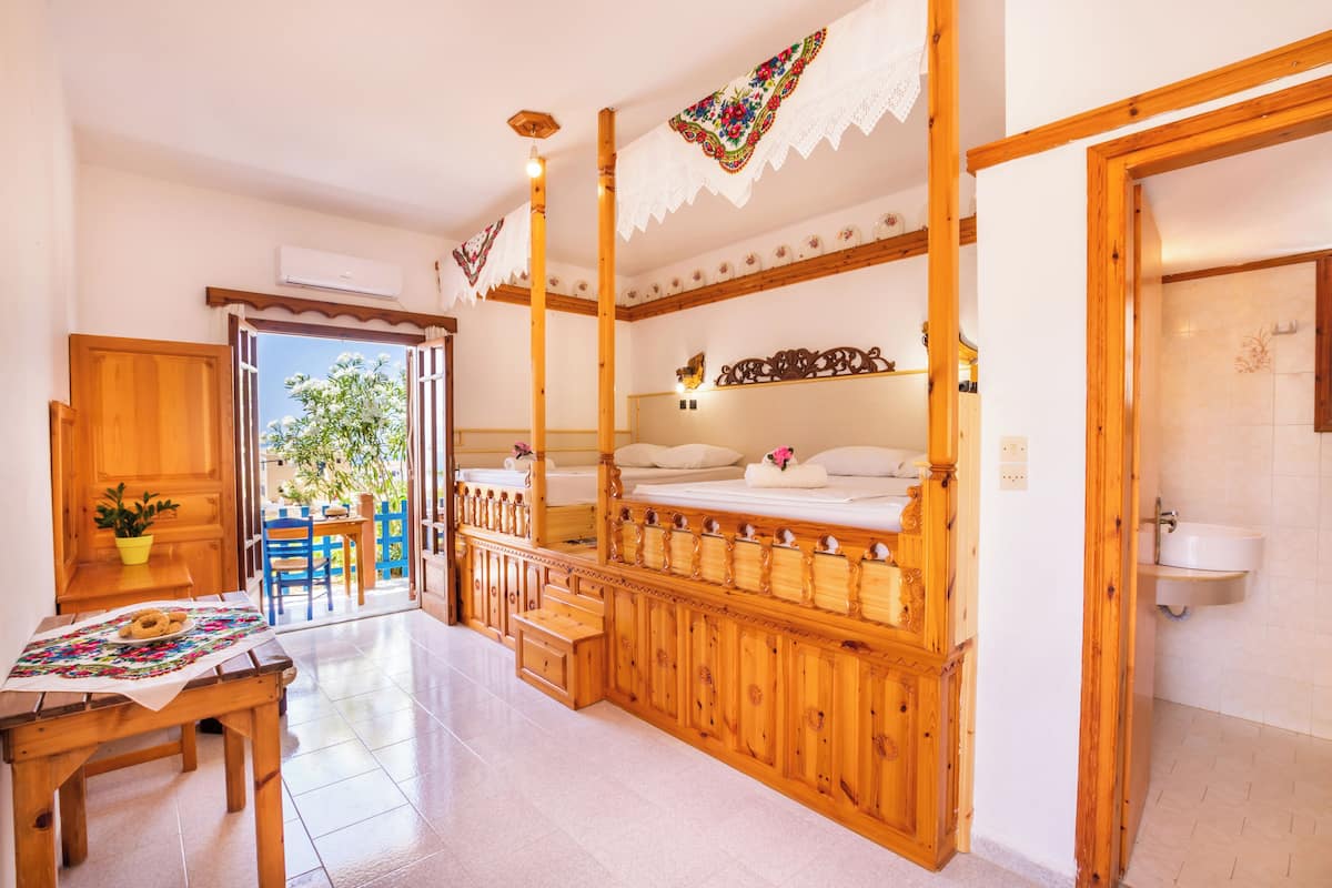 Una habitación con una cama de madera, un baño con lavamanos y un comedor con mesa y sillas.