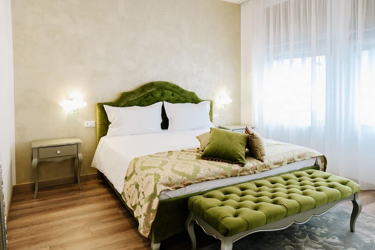 A neatly arranged bedroom with a green upholstered headboard, a matching bench, and a patterned bedspread.