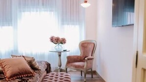 A bedroom with a bed, a bench, a chair, a small table with flowers, and a TV on the wall. - Casa Gallo-Adults Only Sibiu (Sibiu)