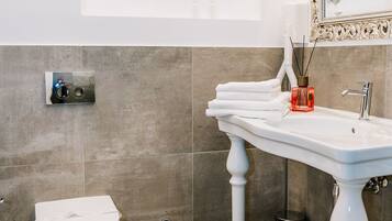Een badkamer met een wit wastafel, een toilet, een spiegel met een sierlijk lijstwerk en een decoratieve hartvormige wanddecoratie.