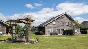 Une maison moderne avec une façade en bois, un patio couvert doté d’une balançoire et une pelouse bien entretenue.