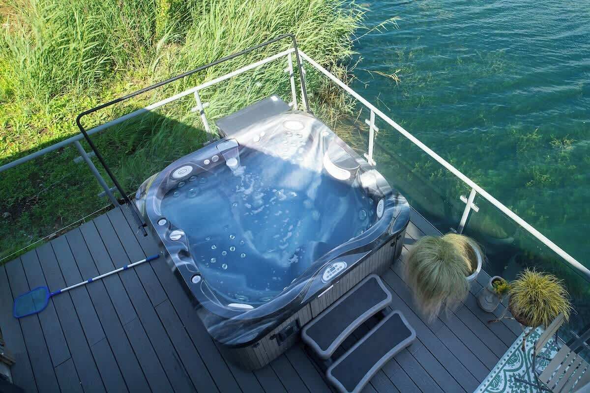 A hot tub on a deck with a railing, surrounded by water and greenery.