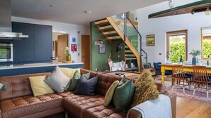 Un salon moderne avec un canapé en cuir marron, un coin repas avec des chaises jaunes et un escalier menant à un niveau supérieur.