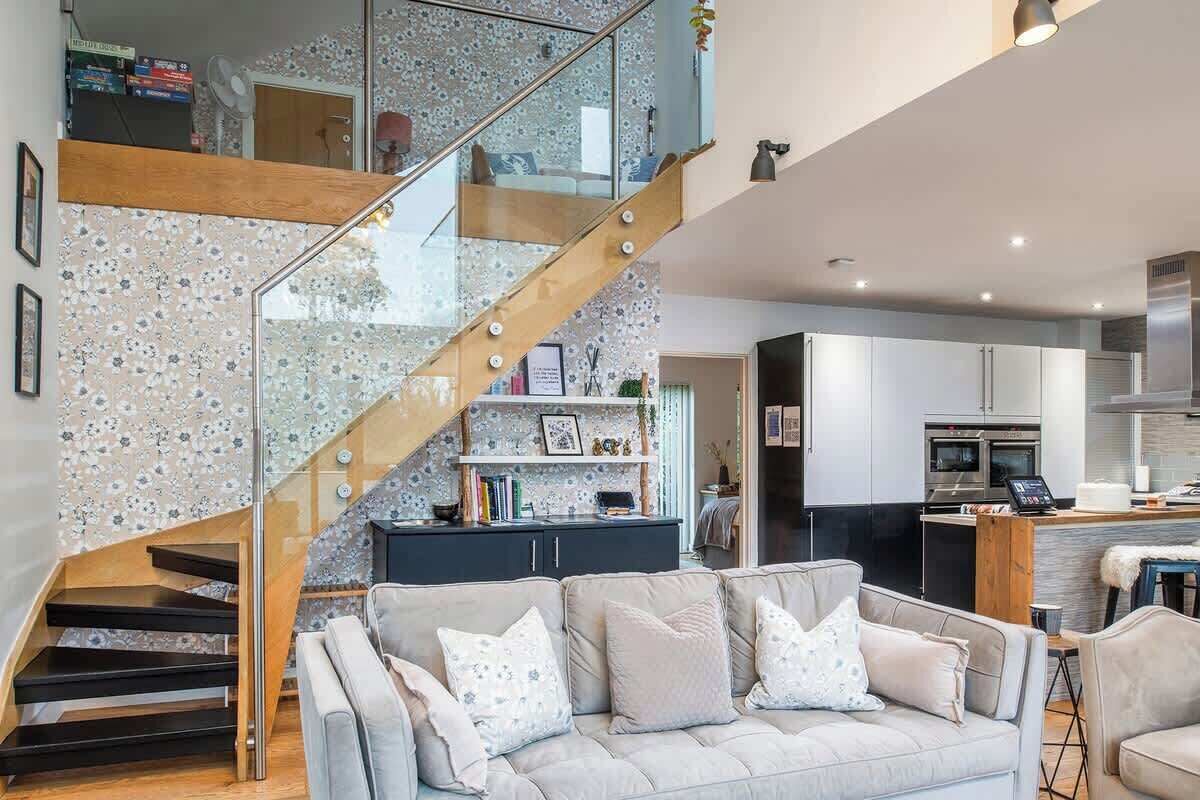 A modern kitchen with stainless steel appliances, a wooden staircase, and a living area with a sofa and decorative pillows.