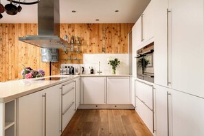Une cuisine moderne avec des armoires blanches, des murs recouverts de panneaux en bois et une hotte de cuisine en acier inoxydable.