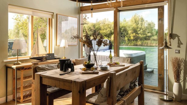 Een houten eettafel met stoelen, een laptop en een vaas met takken.