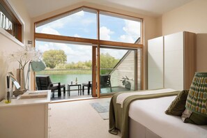 A bedroom with a large sliding glass door leading to a balcony with a view of a body of water and trees.