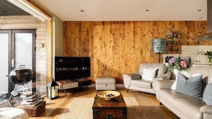 Een moderne woonkamer met een houten wand, een bank, een salontafel, een televisietoestel en een open haard.
