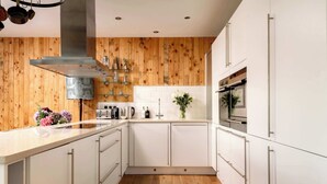 Een moderne keuken met witte kastjes, houten lambrisering en een roestvrijstalen afzuigkap.