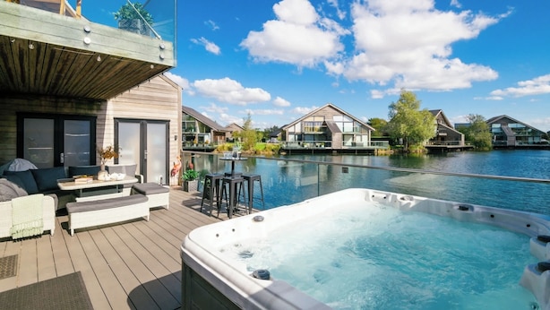 A poolside area with a hot tub, outdoor seating, and a view of the water. - Grebe Lodge (South Cerney)