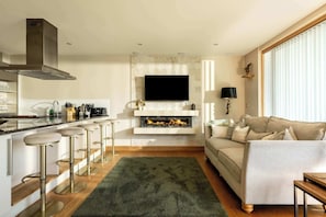 A modern kitchen with a built-in stove, bar stools, and a flat-screen TV mounted above the fireplace.
