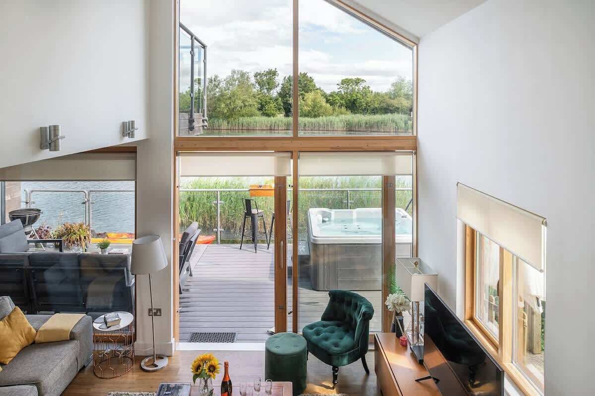 Un salón espacioso con un amplio ventanal corredera que da a una terraza, un rincón de descanso con sofá y sillones, y un televisor sobre un mueble.