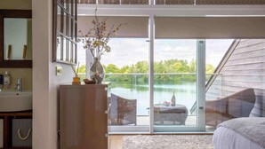 Ein Schlafzimmer mit einem großen Schiebeglasfenster, das auf einen Balkon mit Blick auf einen See führt.