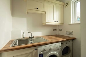 A compact kitchen with a built-in washing machine, a sink, and wooden countertops. - Malachite Lodge (South Cerney)