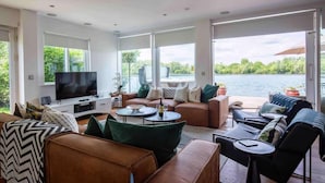 Ein modernes Wohnzimmer mit großem Fernseher, bequemen Sitzgelegenheiten und Blick auf einen See.