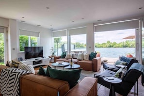 A modern living room with a large TV, comfortable seating, and a view of a lake.