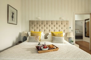 A hotel room with a large bed, two bedside lamps, a framed picture on the wall, and a tray with food on the bed.