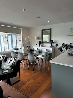 A modern kitchen with a dining area, wooden flooring, and a large window.