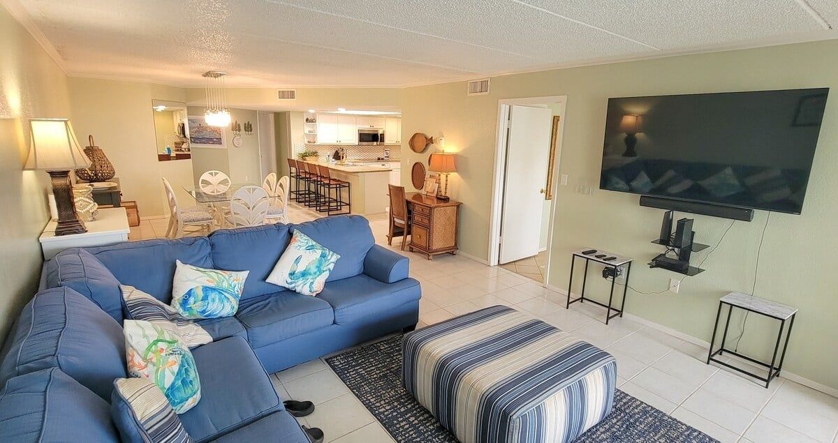 A living room with a sofa, ottoman, TV, and a dining area with chairs and a table.