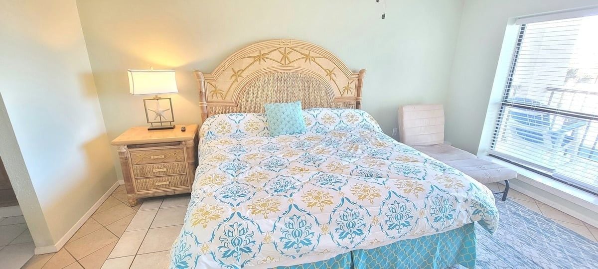 Un dormitorio con cama, mesita de noche, lámpara y ventana con persianas.