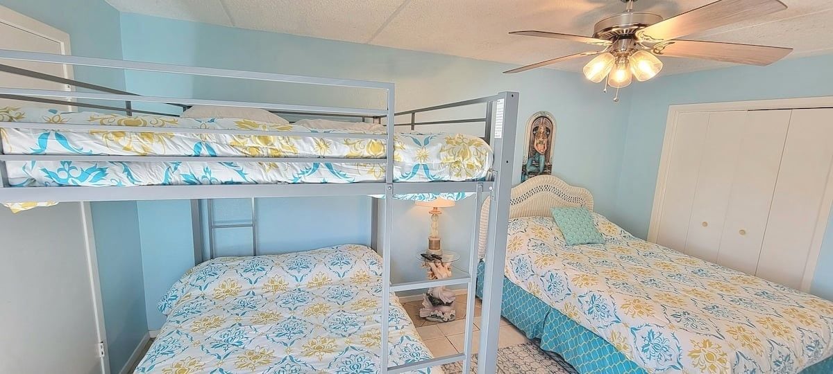 Camera con letto a castello, ventilatore a soffitto, comodino e lampada.