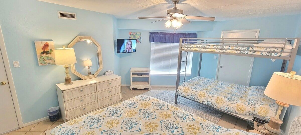 Een slaapkamer met stapelbedden, een dressoir, een televisie en een plafondventilator.