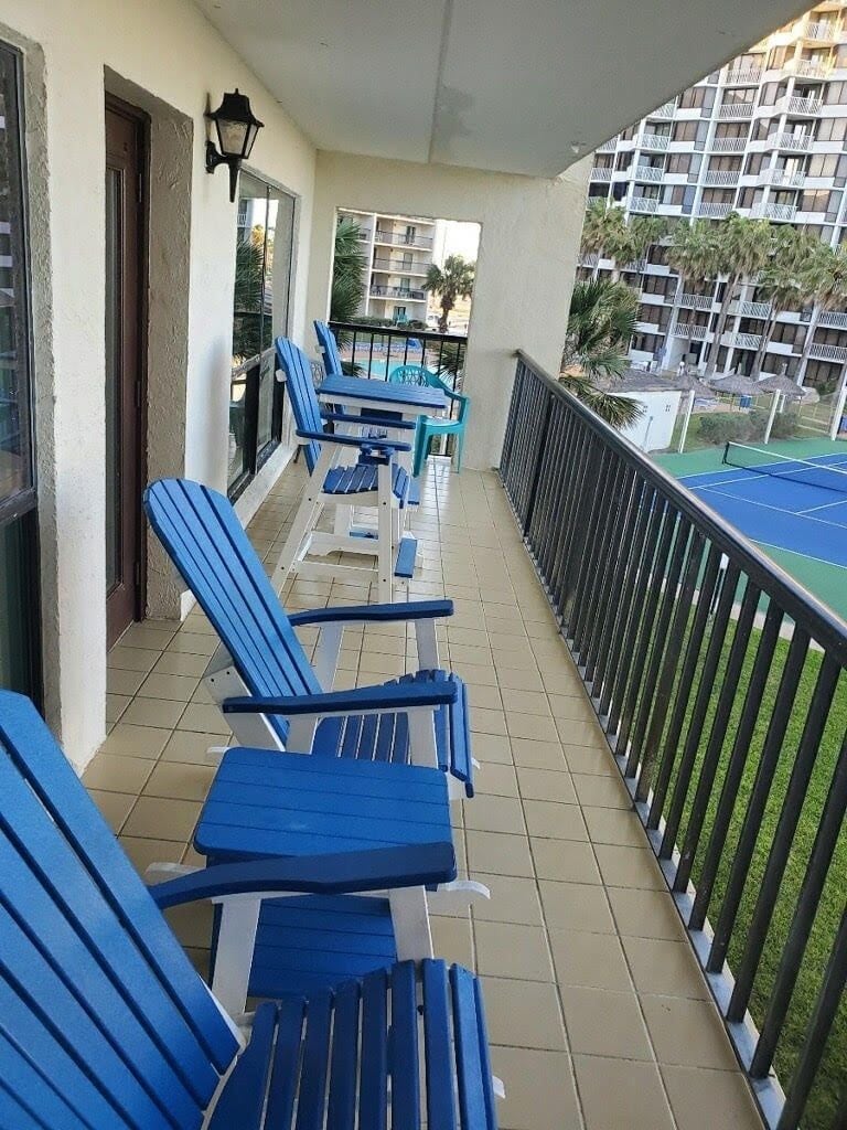 A balcony with blue chairs, a tiled floor, and a view of a building with balconies.