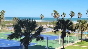 Pista de tenis con piscina y palmeras, con vista al océano.