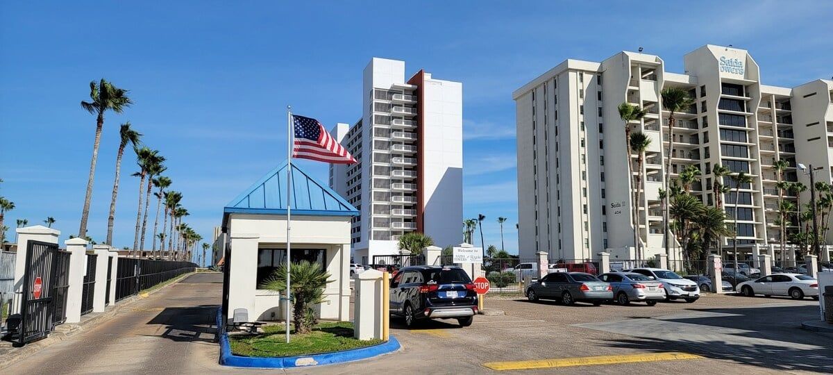 Entrada de hotel con techo azul, una bandera estadounidense y un estacionamiento con coches.