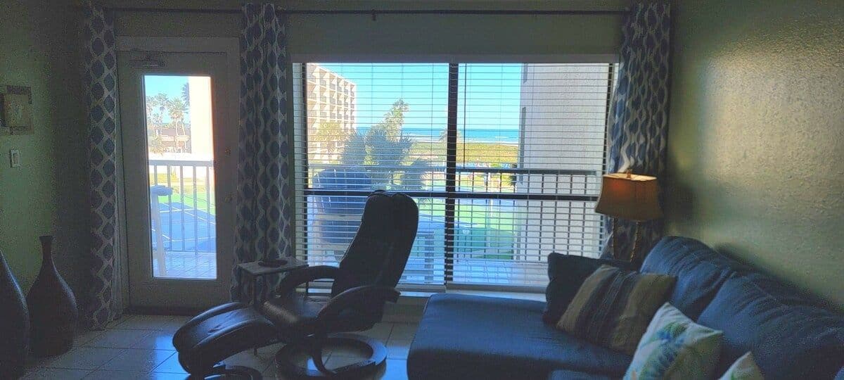 Una habitación con un ventanal grande, un sofá, una silla y una lámpara.