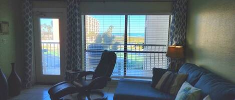 Una habitación con un ventanal grande, un sofá, una silla y una lámpara.