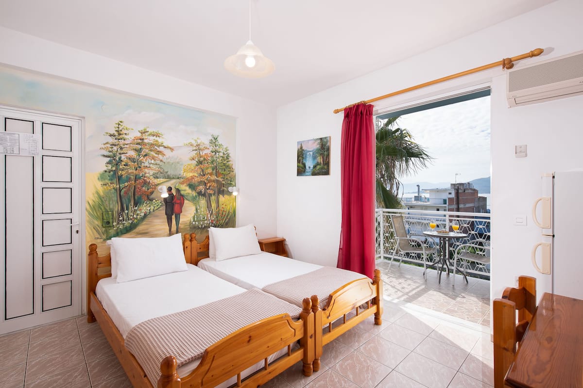 A double bed with a wooden headboard, a small bedside table, and a painting of a landscape on the wall.