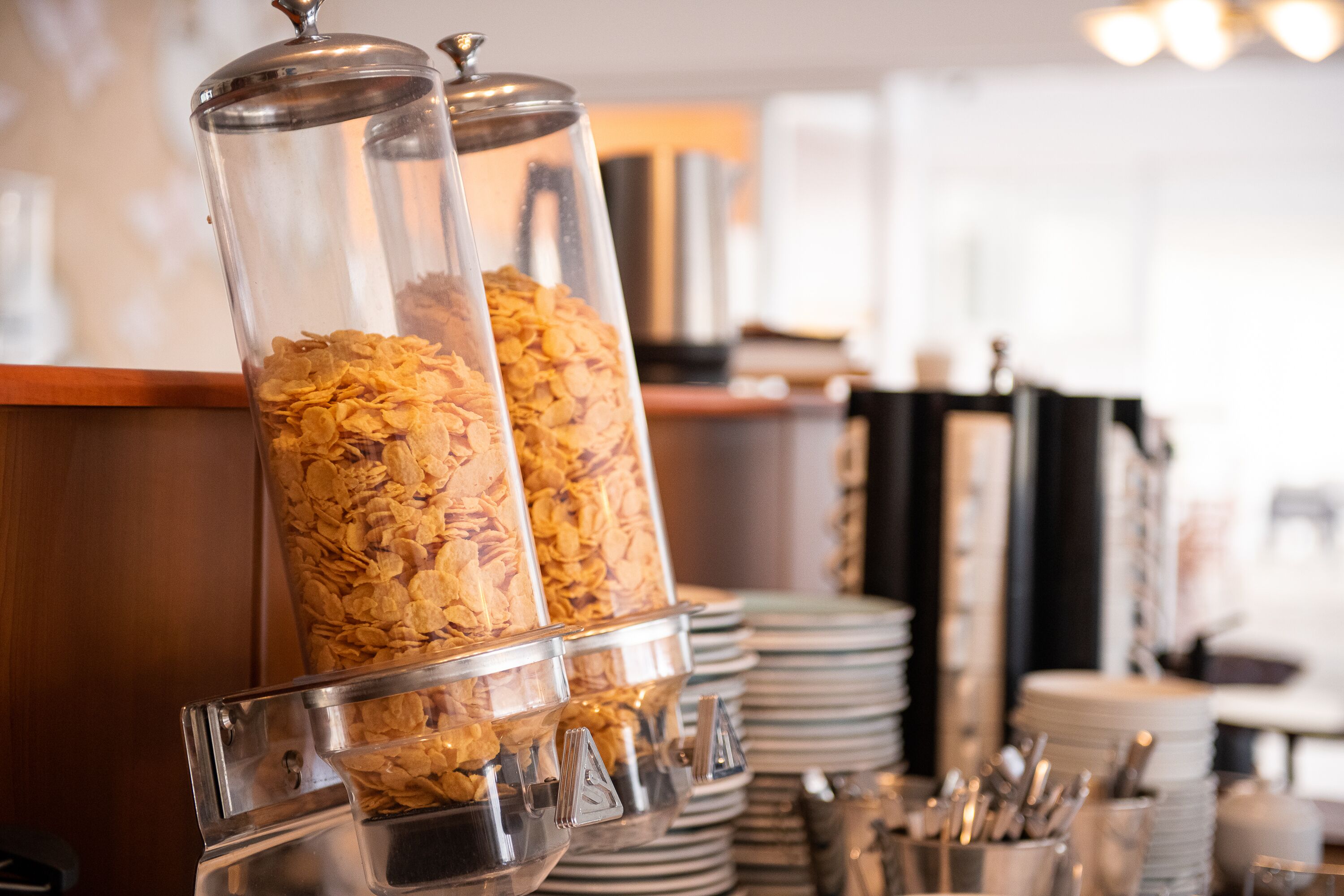Una barra de desayuno con dispensadores de cereales y platos apilados.