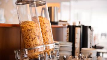 Una barra de desayuno con dispensadores de cereales y platos apilados.