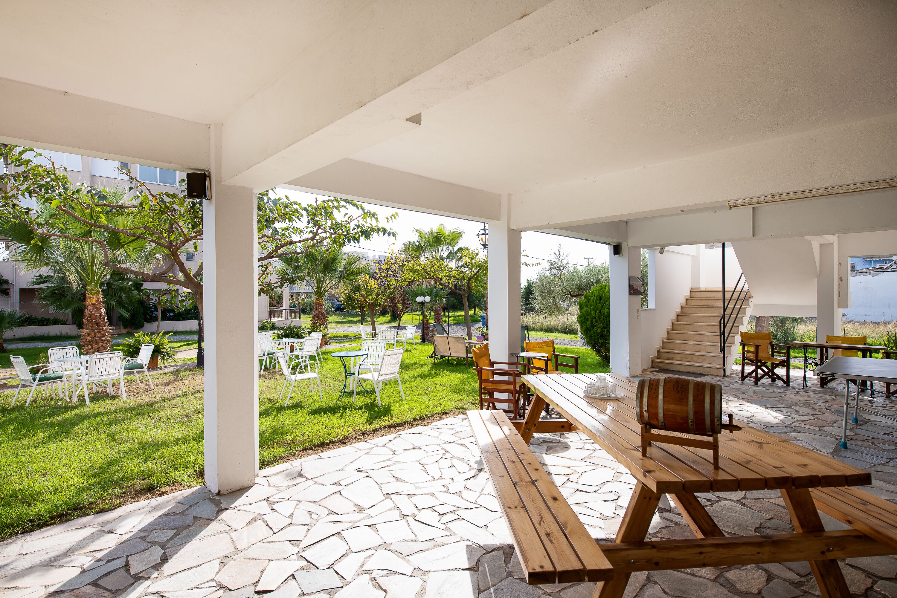 An outdoor patio with stone flooring, wooden benches, and white chairs.