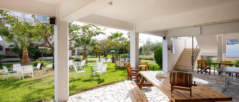 An outdoor patio with stone flooring, wooden benches, and white chairs.