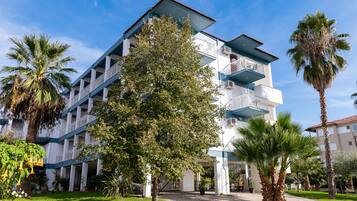 Ein mehrstöckiges Hotel mit Balkonen, umgeben von Palmen und einem gepflegten Rasen.