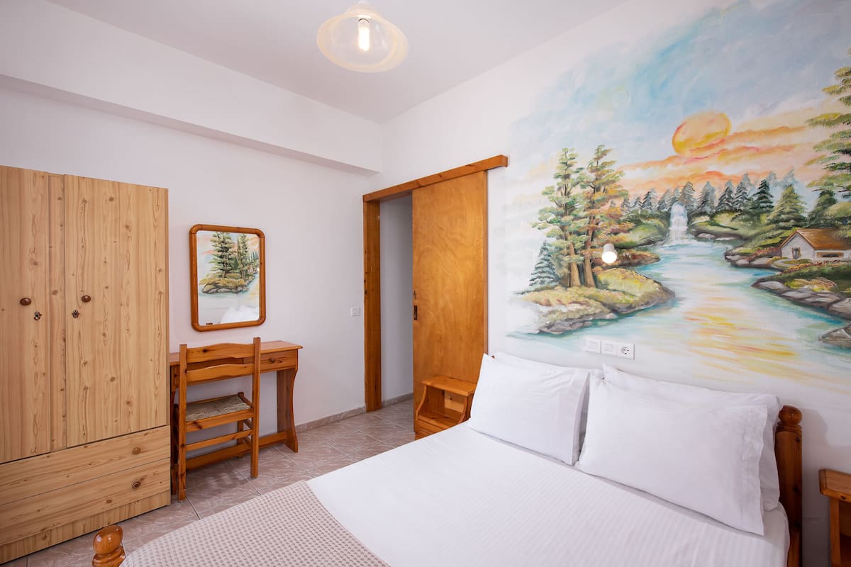 A bedroom with a bed, wooden wardrobe, desk, and chair.
