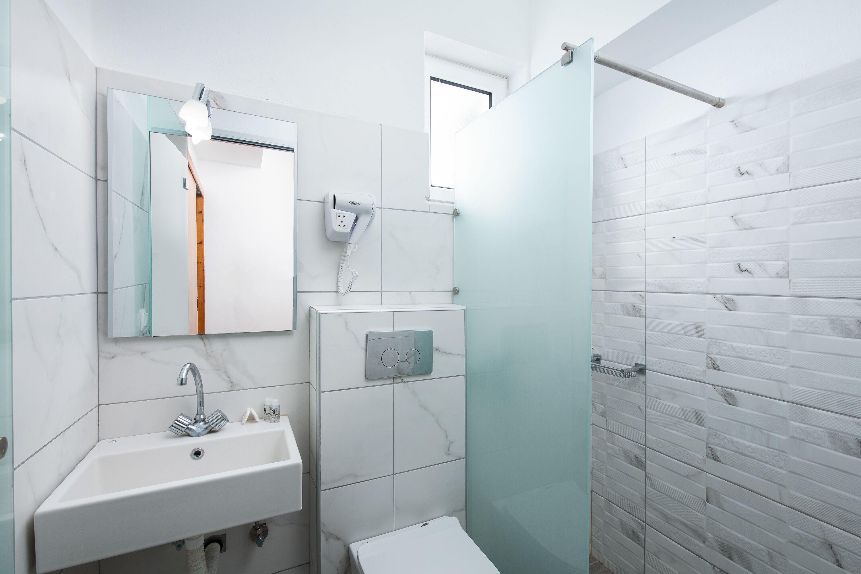 Un baño con lavamanos blanco, espejo, inodoro y ducha con puerta de cristal.