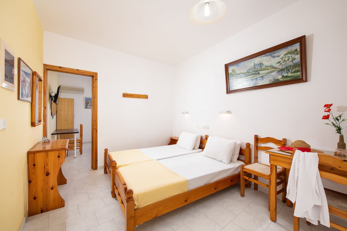 A room with a wooden bed, a desk, a chair, a small table, and a painting on the wall.