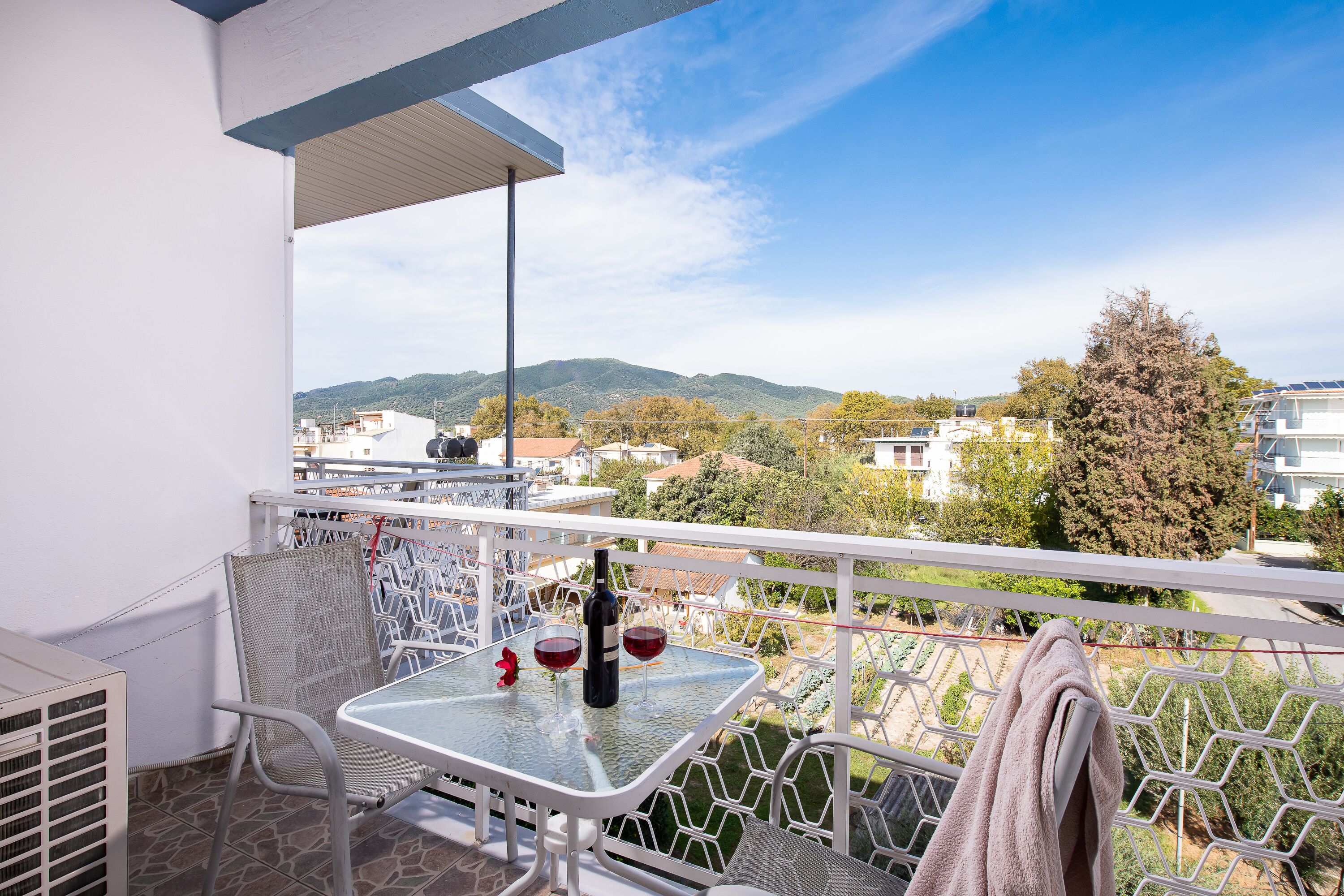 A balcony with a table, two chairs, a bottle of wine, and two wine glasses.