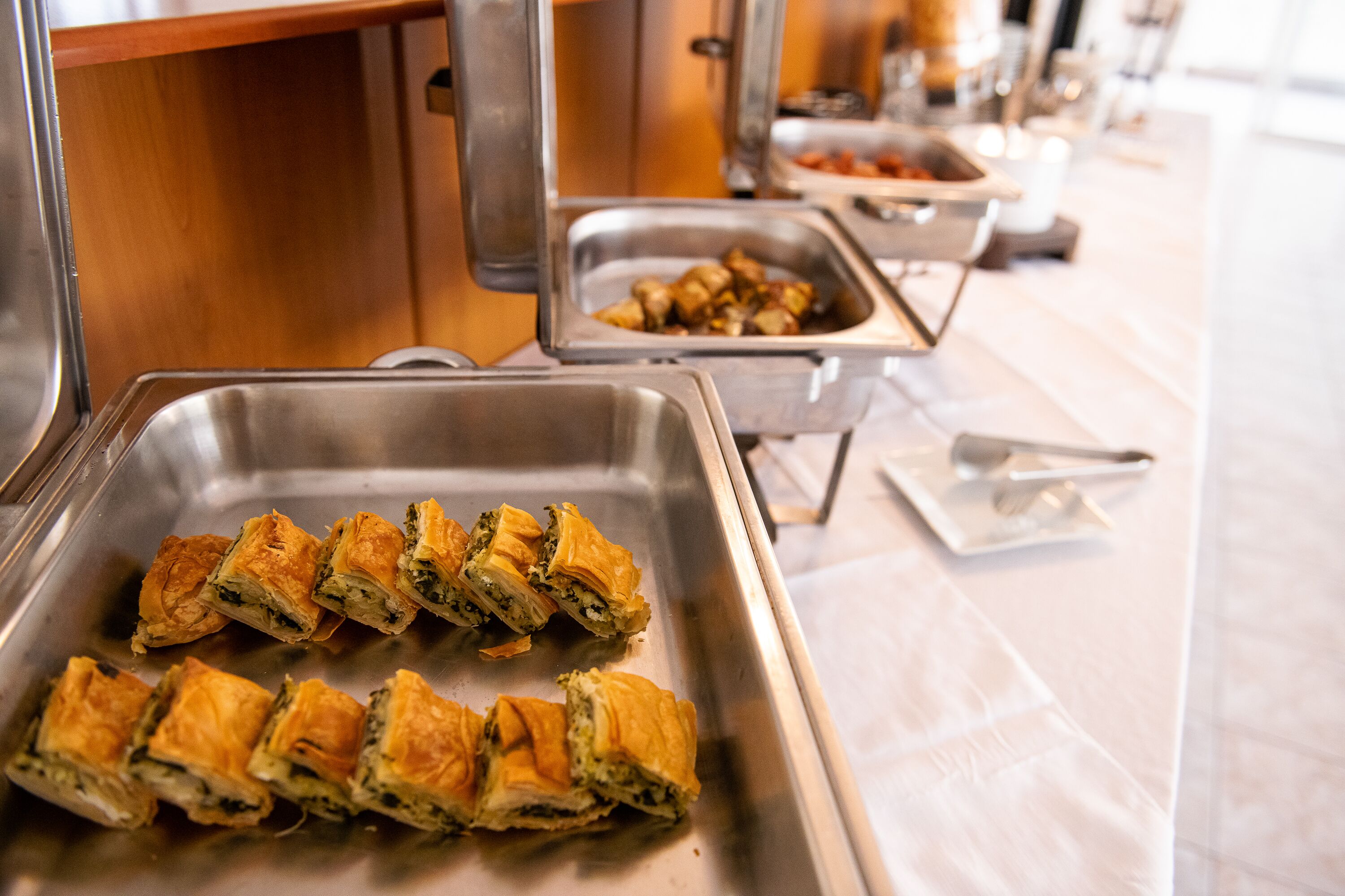 A buffet table with trays of food, including a tray of baked pastries.