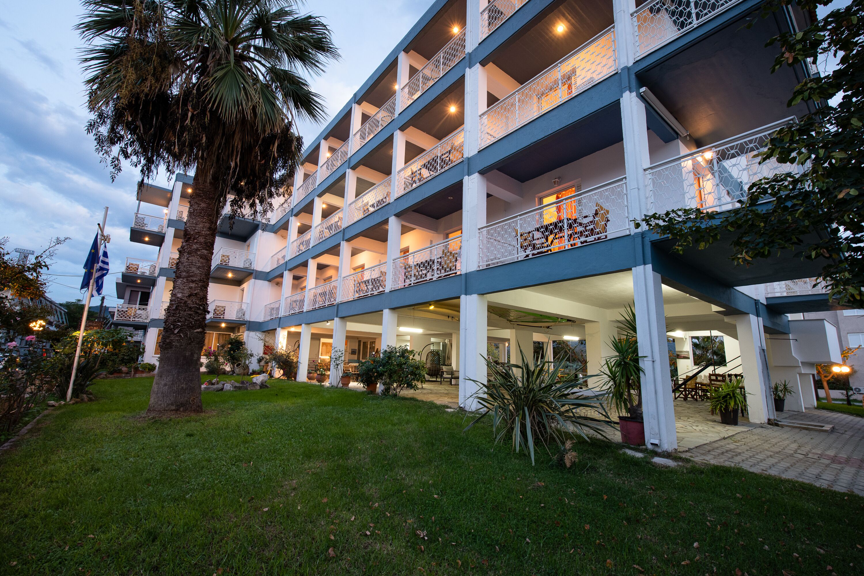 A multi-story hotel with balconies, a covered outdoor area, and a well-maintained garden.