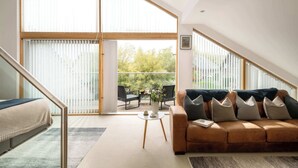 Ein modernes Wohnzimmer mit einem großen Schiebeglasfenster, das auf einen Balkon führt, ein braunes Ledersofa, ein kleiner runder Couchtisch und eine Treppe.