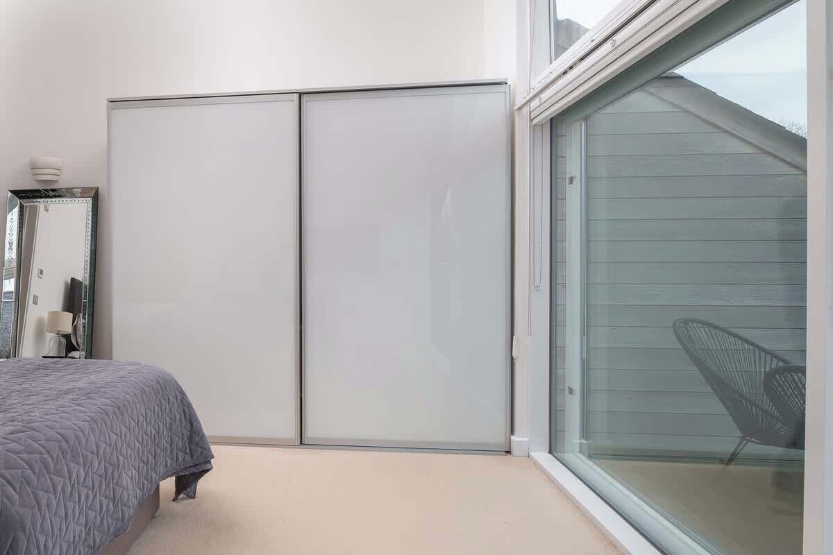 A bedroom with a bed, a wardrobe, a mirror, and a sliding glass door leading to an outdoor area.