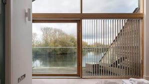 A modern room with a large sliding glass door leading to a balcony overlooking a body of water and trees.